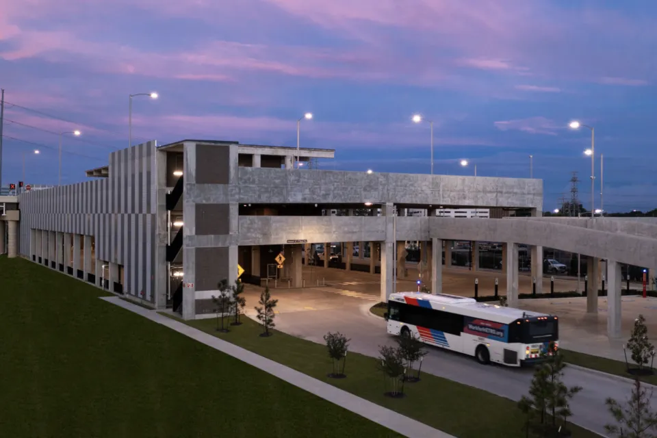 View of Westpark/Lower Uptown transit center in Houston with bus exiting three-story garage vuilding and purple sunset sky in background
